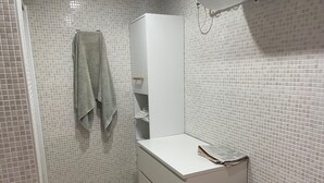 Een badkamer met witte betegelde wanden, een wit kastje met lades, een handdoek aan de muur en een douchegedeelte.