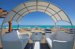 A beachside seating area with white wicker chairs and a table, overlooking the beach and turquoise waters. - Seaview apartment in  hotel Gravity Sahl Hasheesh/heated pool/Buki-Gravity-Homes (Hurghada, Red Sea Governorate)