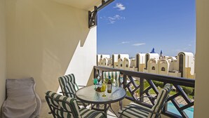 Un balcon avec une table ronde et des chaises à rayures, donnant sur une piscine et présentant une architecture traditionnelle.