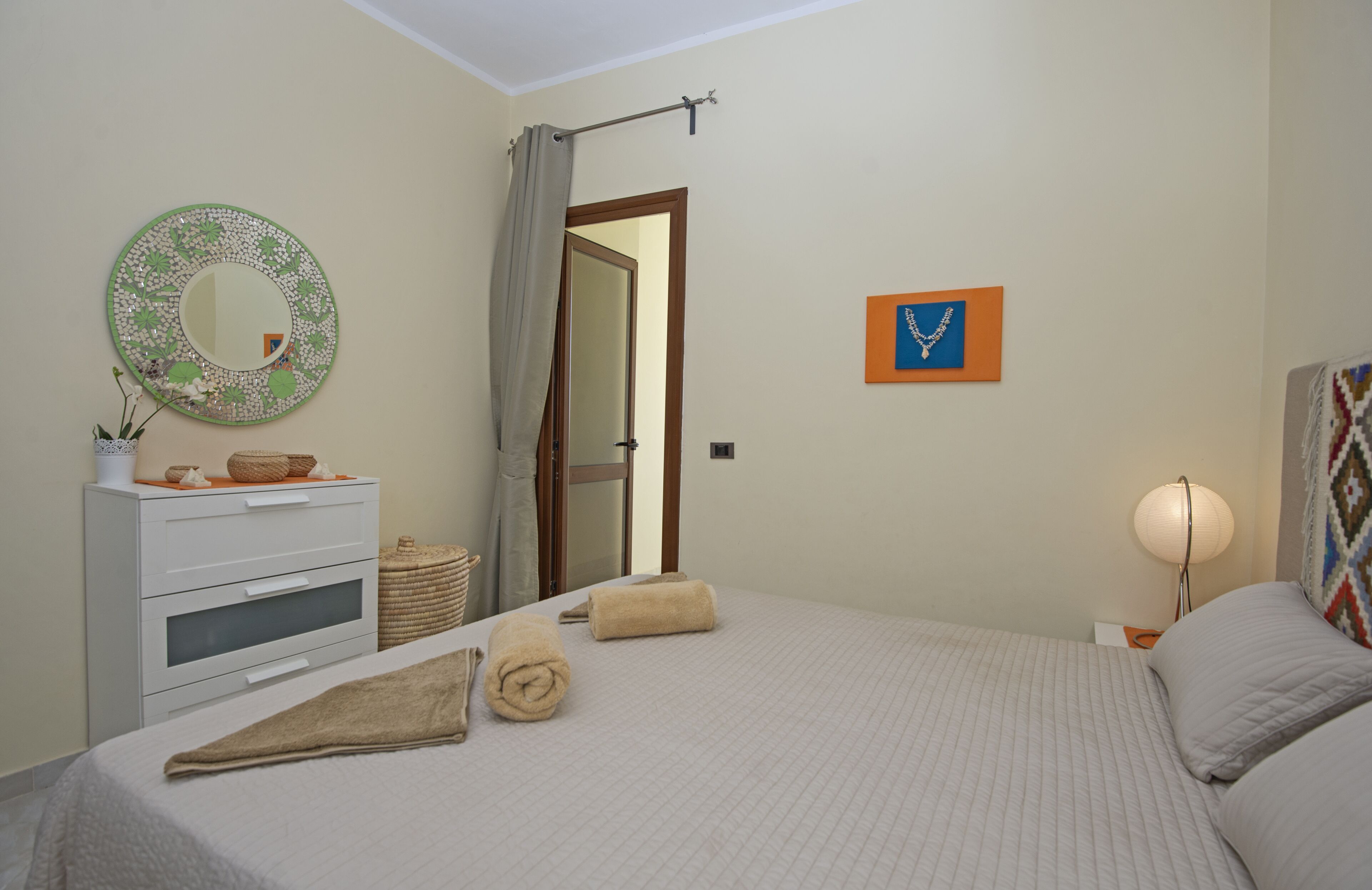 Une chambre à coucher comprenant un lit, une commode, un miroir, un tableau encadré et une lampe.