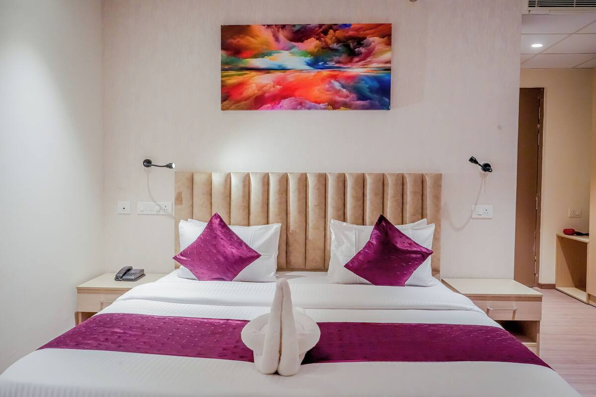 Habitación de hotel con una cama grande, dos mesitas de noche, un teléfono y un cuadro en la pared.