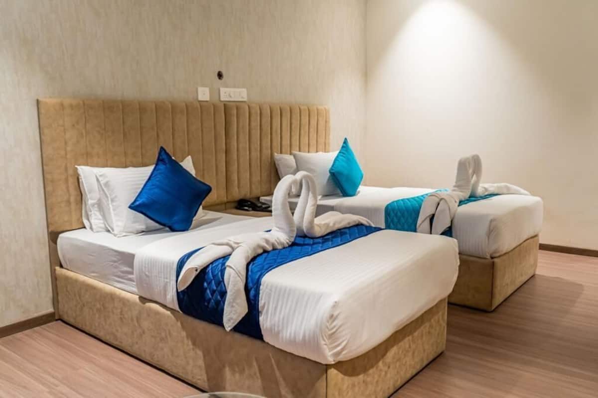 Habitación de hotel con dos camas, cada una con cabecera, ropa de cama blanca y almohadas azules y blancas.
