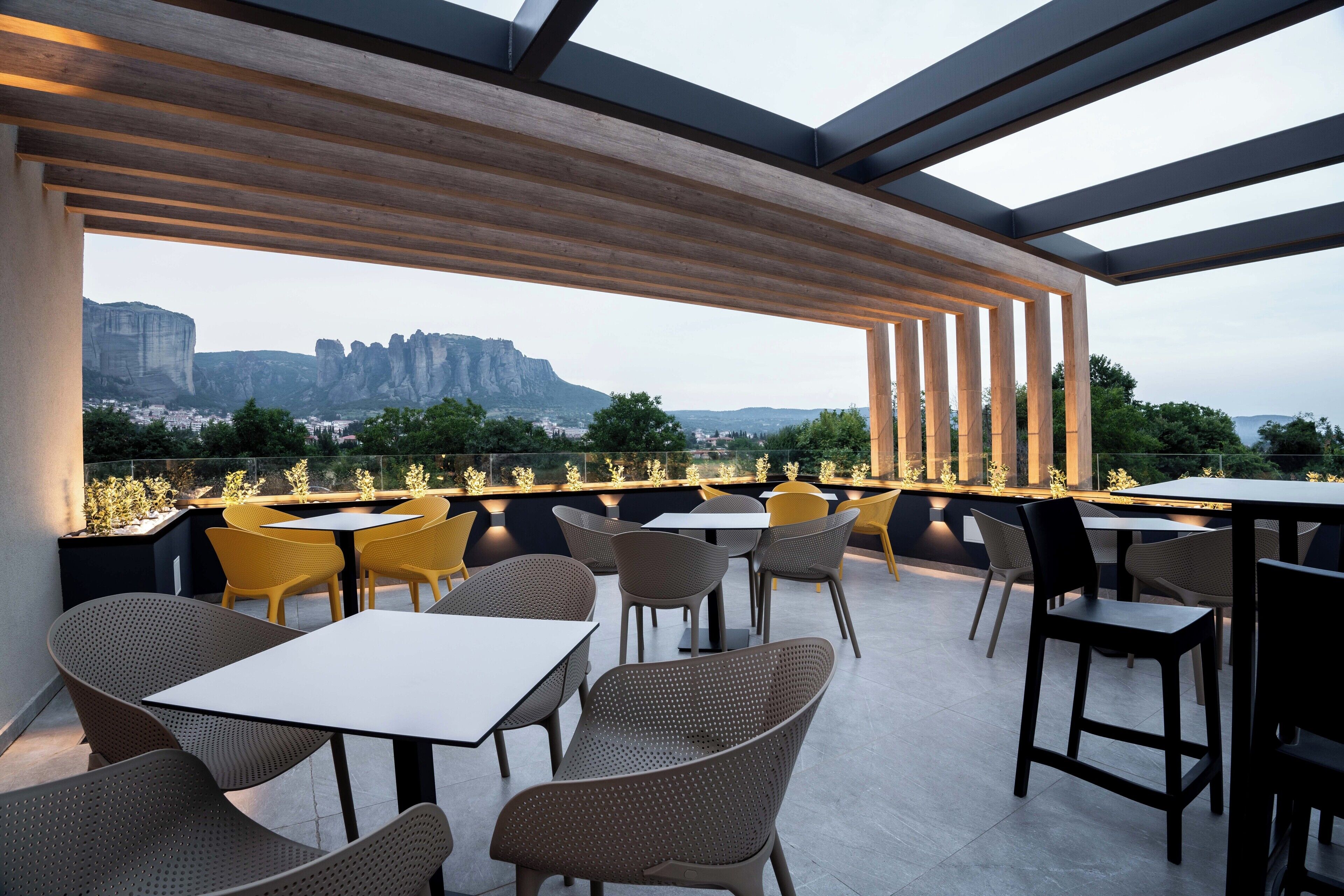 An outdoor seating area with tables and chairs, overlooking a scenic view of cliffs and greenery.