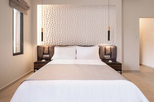 A modern hotel room with a large bed, two bedside tables, and a textured wall behind the bed.