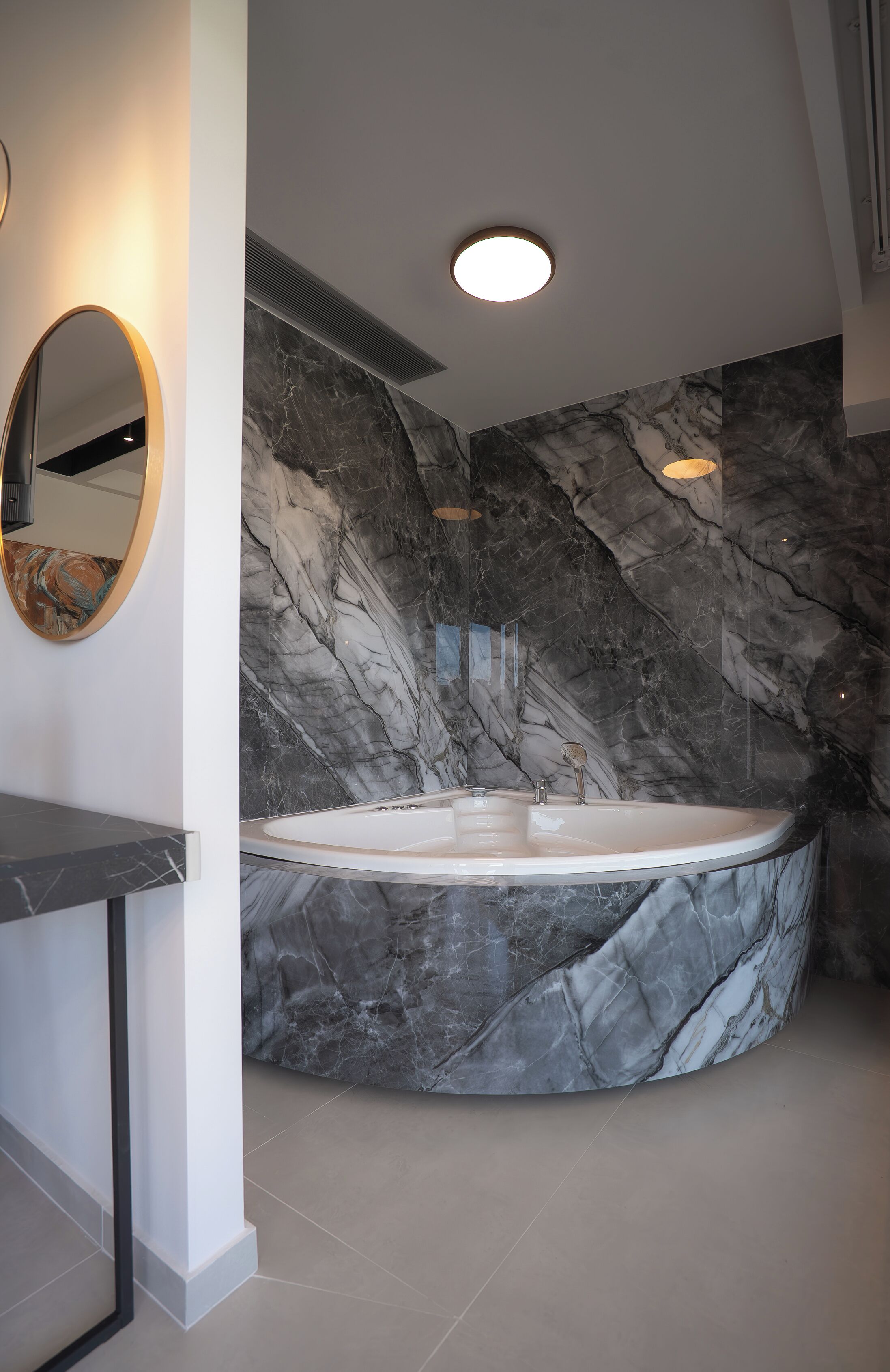 Une salle de bain moderne avec un mur en marbre, un miroir rond et une baignoire sur pieds.