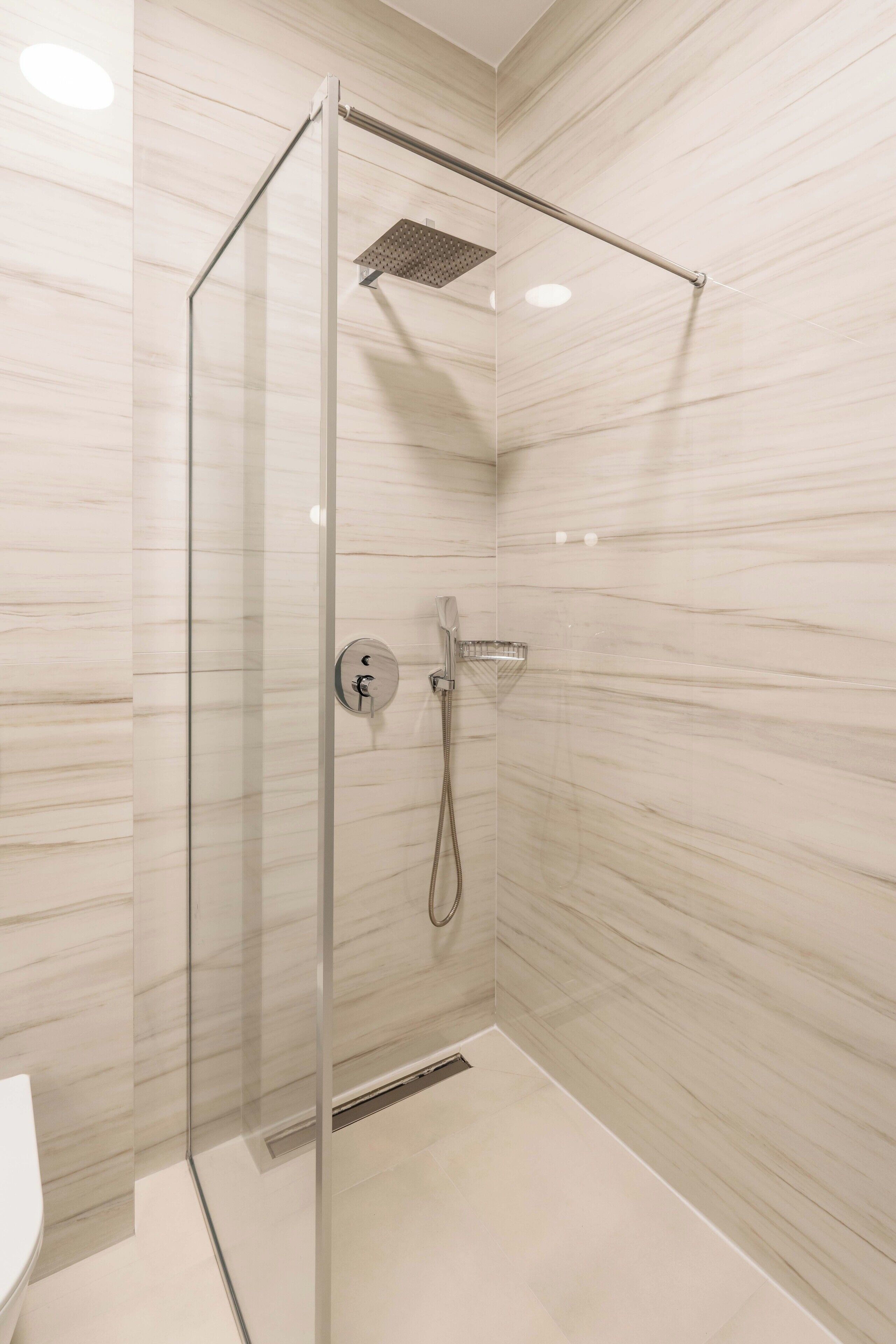 Une douche fermée par des parois en verre, dotée d’un pommeau de douche à main et d’un panneau de commande fixé au mur.