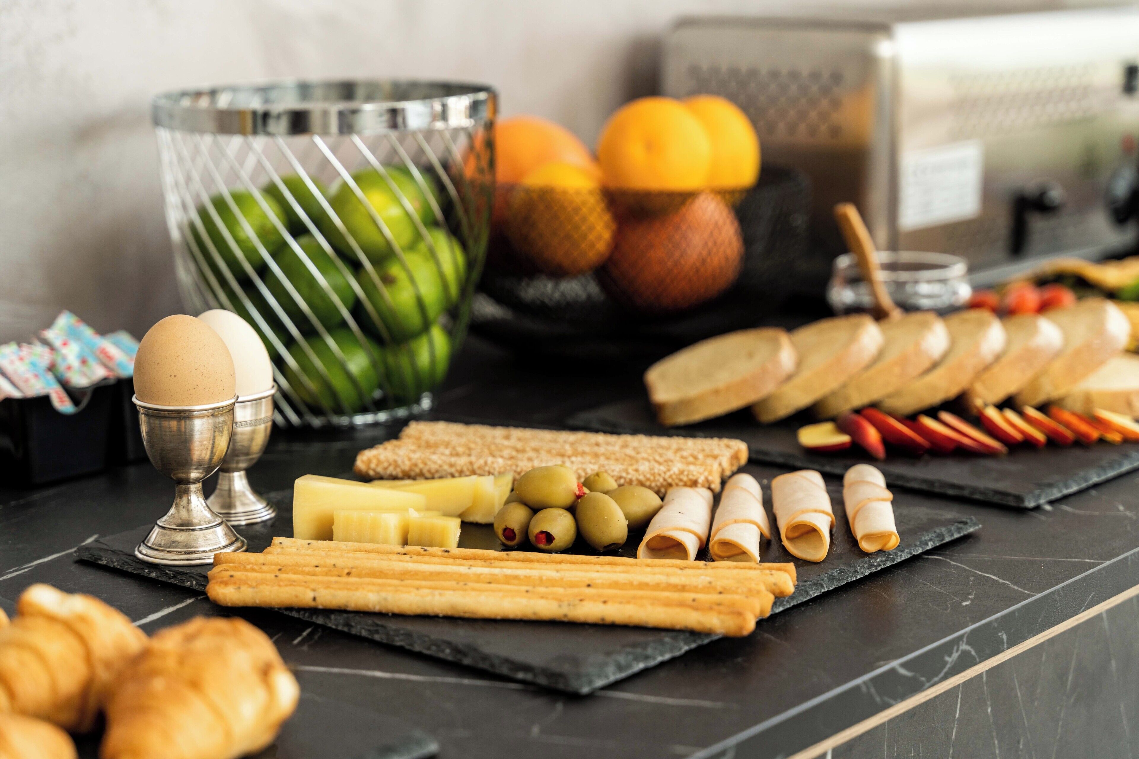 A variety of food items including bread, cheese, olives, and eggs on a black marble table.