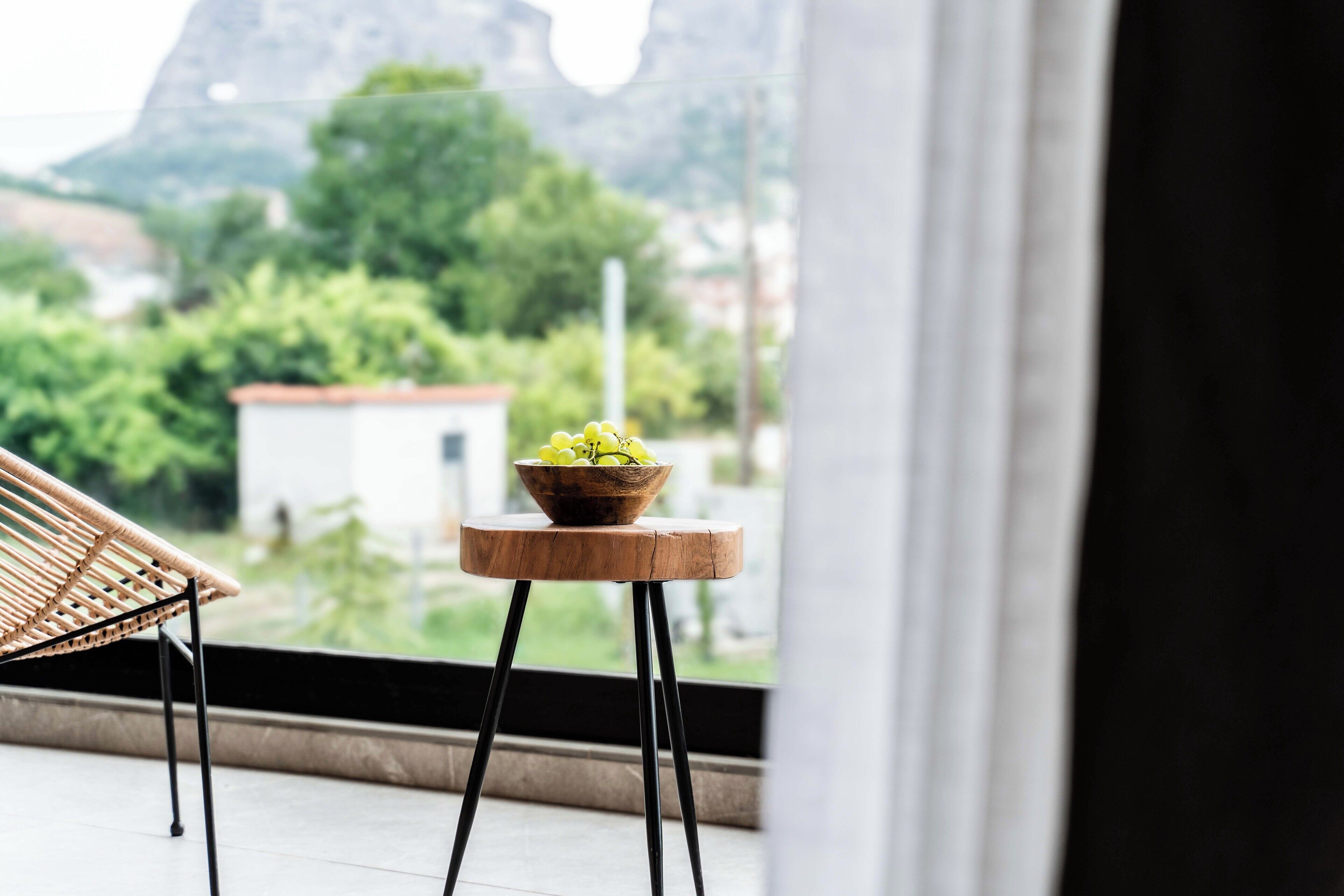 Une vue depuis un balcon, avec une chaise en osier et un tabouret en bois sur lequel est posé un vase rempli de fleurs jaunes.