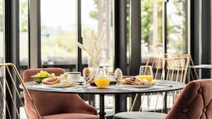 A breakfast table set with eggs, toast, fruit, and orange juice in a modern dining area with large windows and metal chairs.