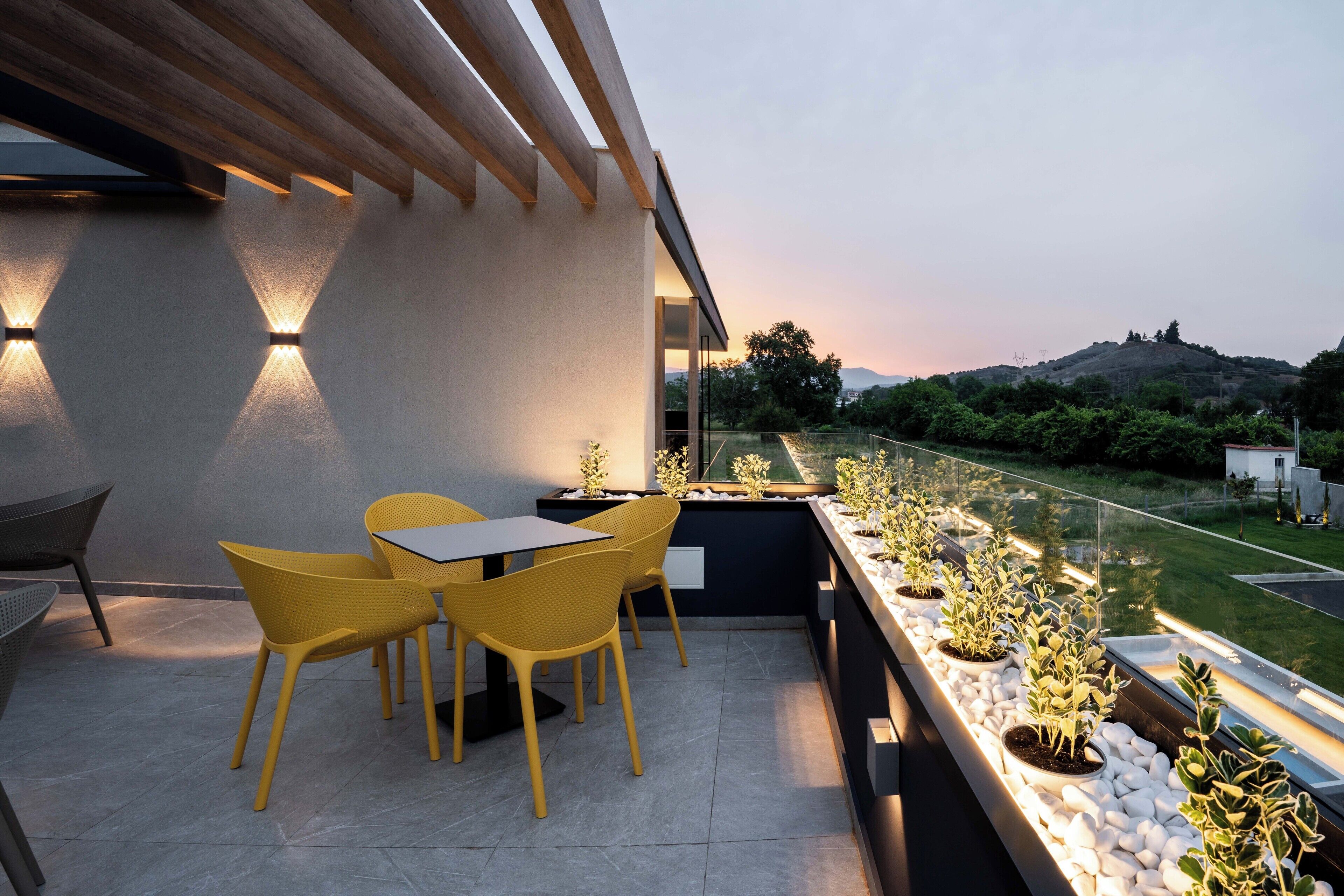 Eine moderne Außenpatio mit gelben Stühlen und einem Tisch, einer Glasumlaufung und Kübelpflanzen.