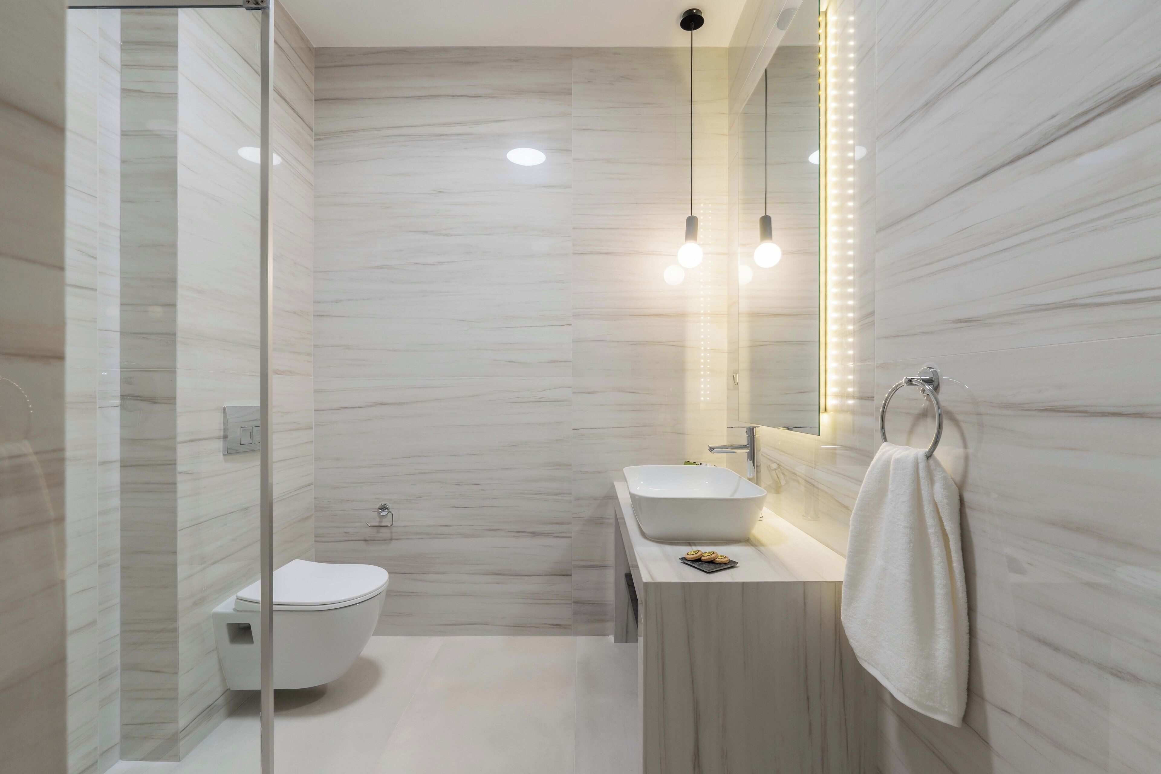 Ein modernes Badezimmer mit Duschkabine aus Glas, Toilette, Waschbecken mit Spiegel und einem Handtuch an der Wand.