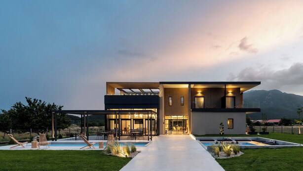 A modern two-story house with a swimming pool, outdoor seating, and a mountain backdrop.