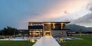 A modern two-story house with a swimming pool, outdoor seating, and a mountain backdrop.