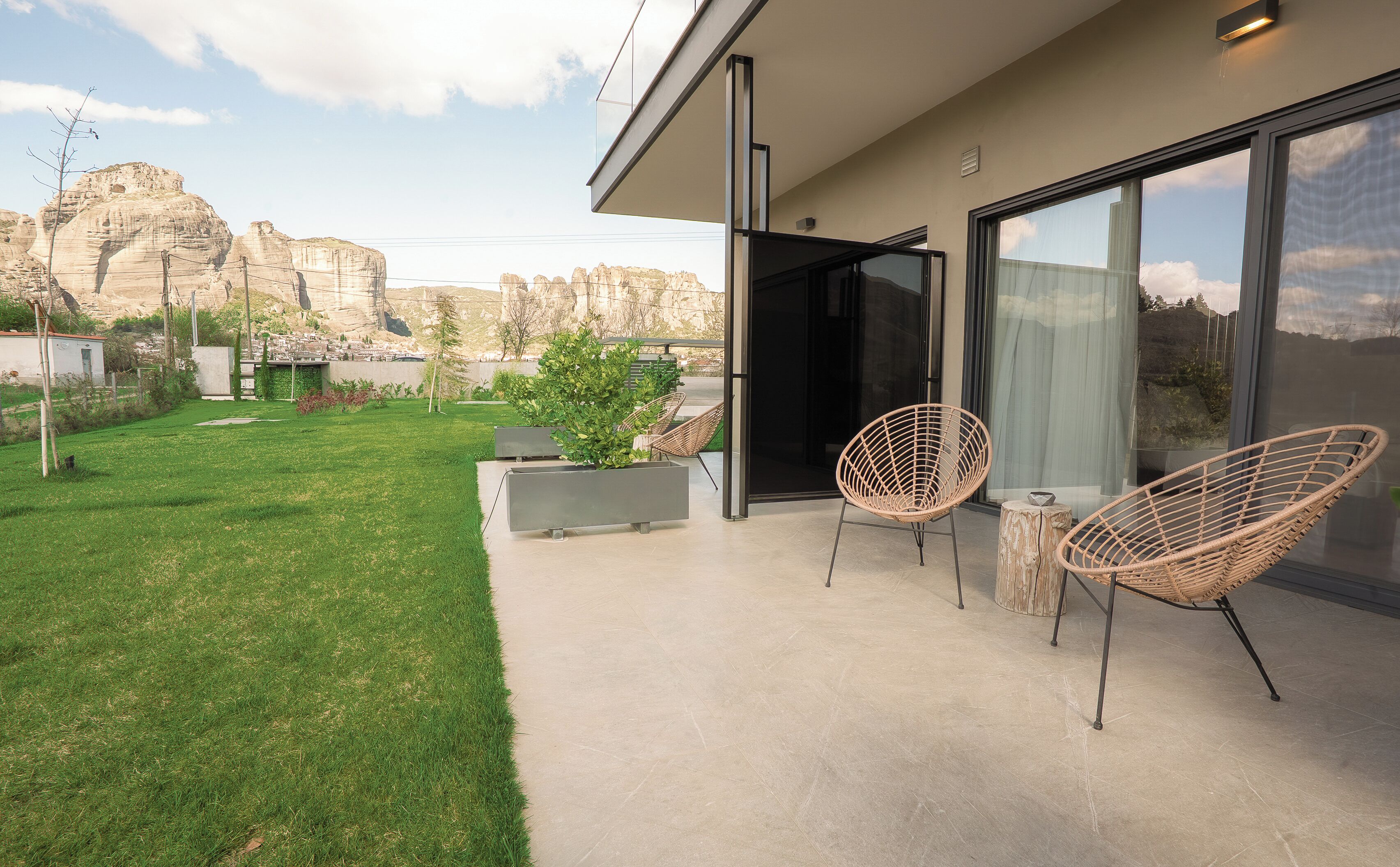 A modern outdoor patio with a clear view of a mountainous landscape, a glass door leading to the interior, and wicker chairs.