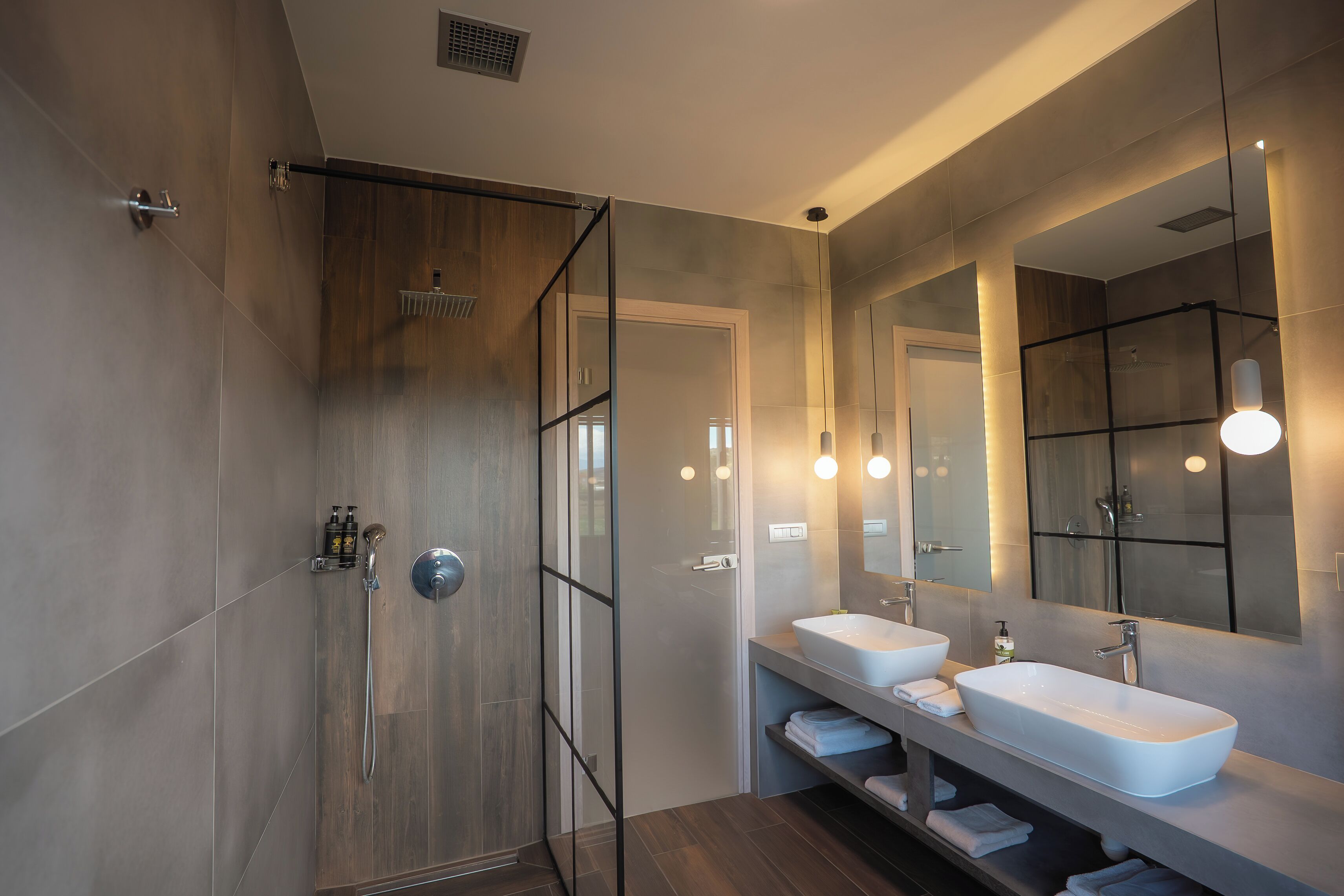 Un baño moderno con cabina de ducha, dos lavabos y un espejo grande.