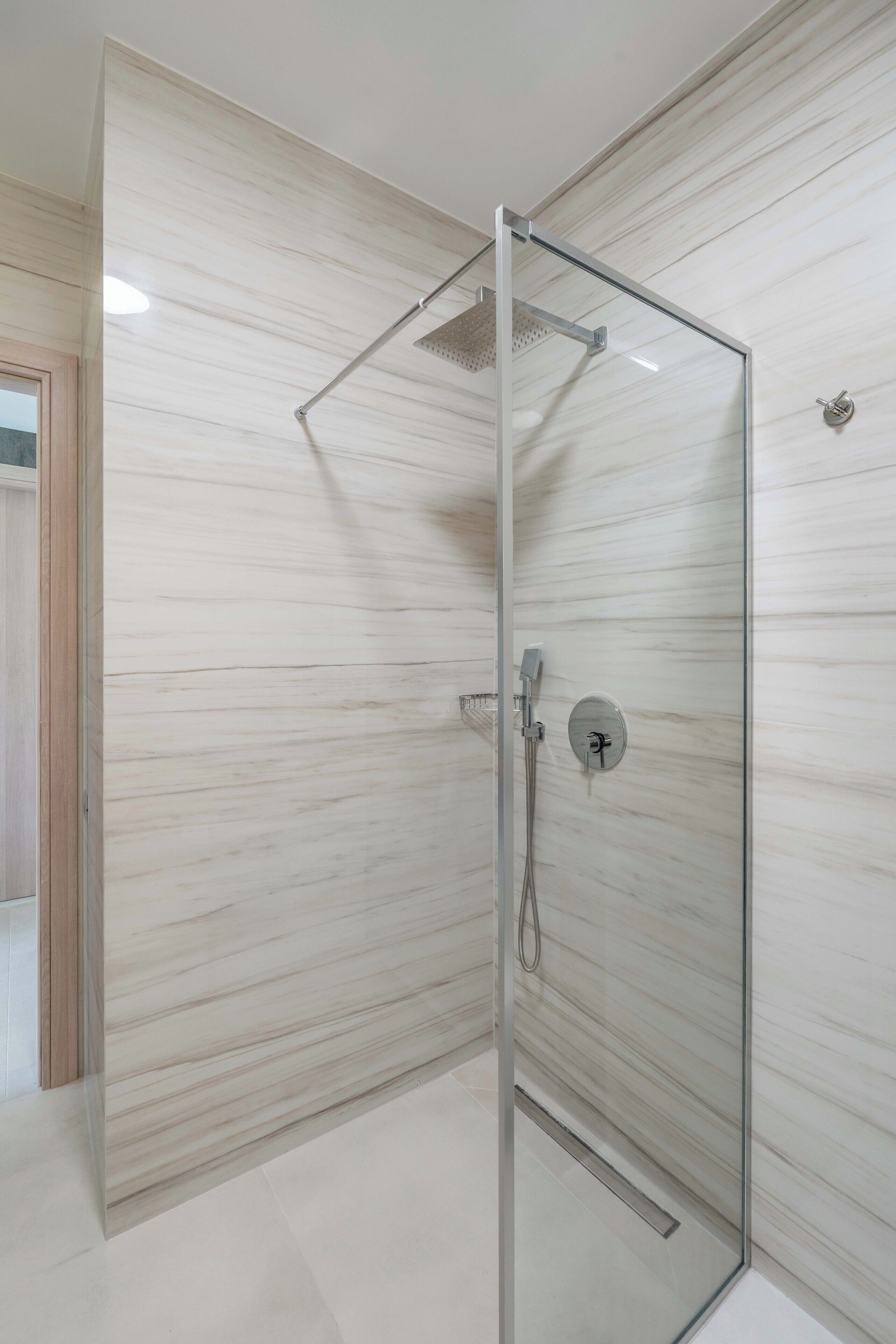 Een moderne badkamer met een douche in glazen cabine, marmeren wanden en een zichtbaar toilet.