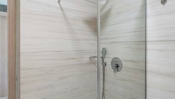 Een moderne badkamer met een douche in glazen cabine, marmeren wanden en een zichtbaar toilet.