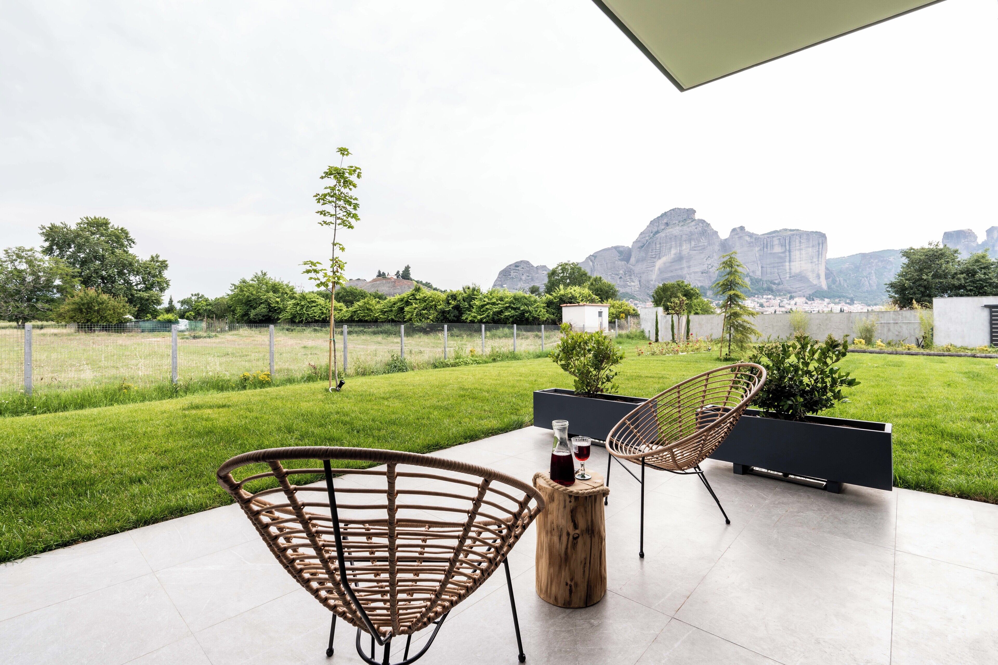 A modern outdoor patio with two wicker chairs, a wooden table, and a black planter.