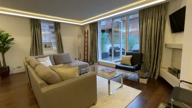 A modern living room with a sofa, a coffee table, and a TV mounted on the wall. - Two Bedroom Flat in Belgravia (London)
