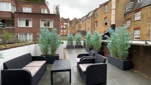 A courtyard with outdoor seating, potted plants, and brick buildings in the background. - Two Bedroom Flat in Belgravia (London)