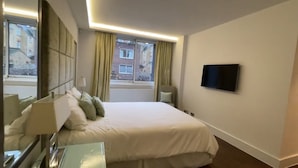 A hotel room with a large bed, a flat-screen TV mounted on the wall, and a window with curtains. - Two Bedroom Flat in Belgravia (London)