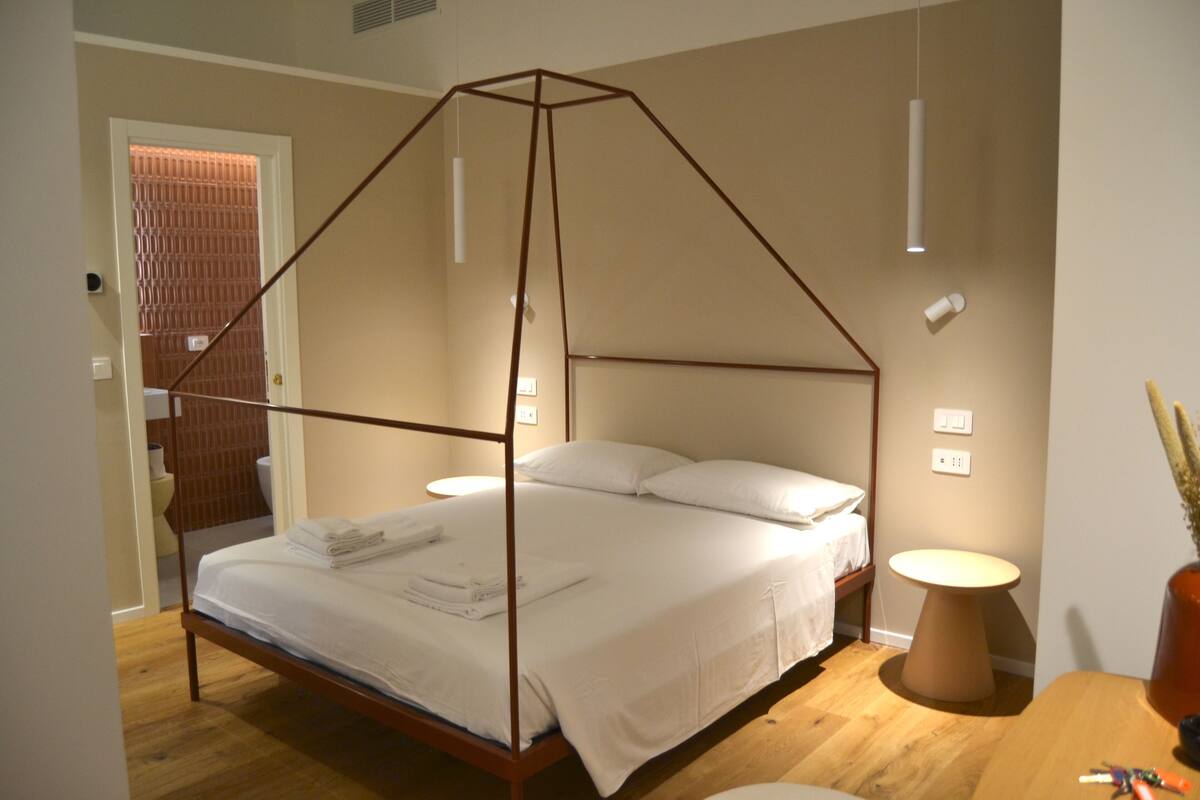 Une chambre à coucher moderne avec un lit à baldaquin, une table de chevet et une petite table ronde sur laquelle se trouve une lampe.