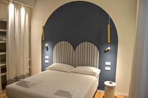 A neatly made bed with white linens, a dark headboard with vertical stripes, and a small bedside table with a white lamp.