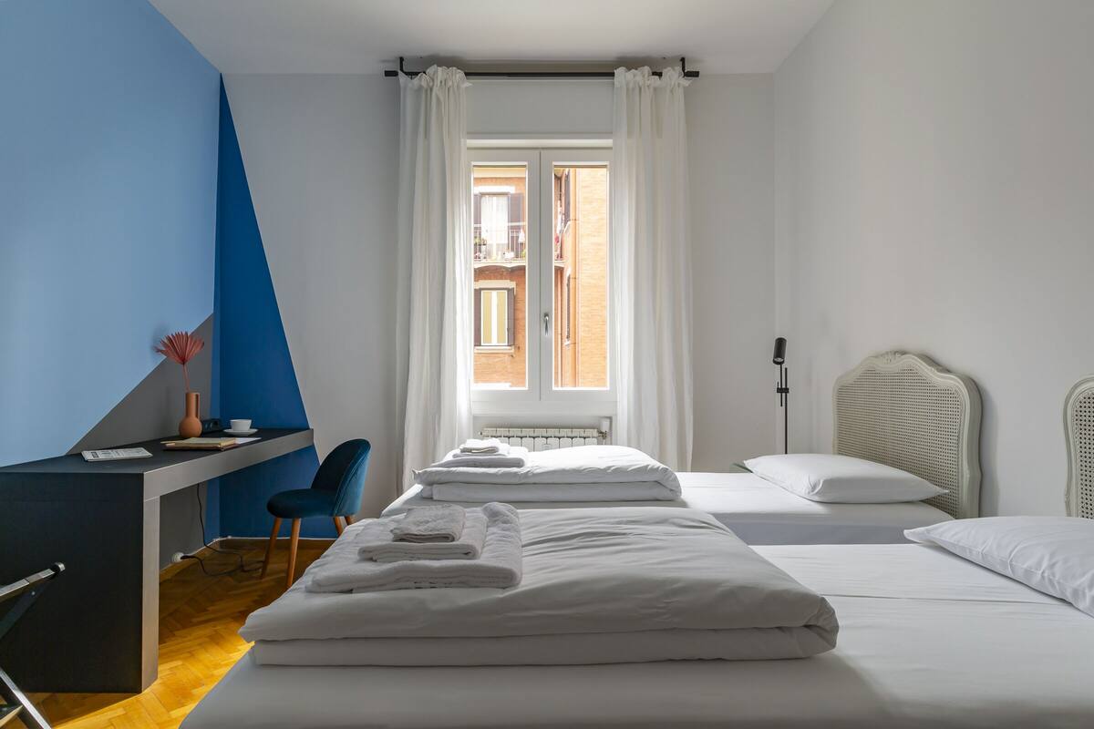 Une chambre d’hôtel équipée d’un bureau, de deux lits, d’une chaise et offrant une vue sur l’extérieur.