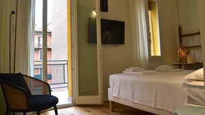 Ein Hotelzimmer mit Bett, Sessel, Fernseher und einem Balkon mit Blick nach außen.