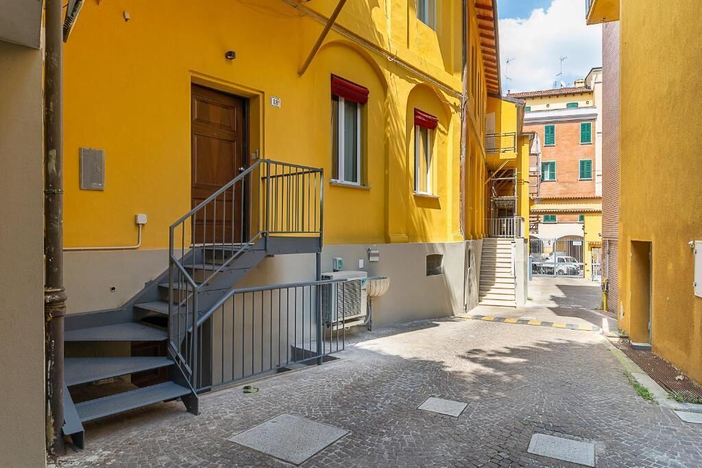 A narrow street with a yellow building, a wooden door, and a metal staircase.
