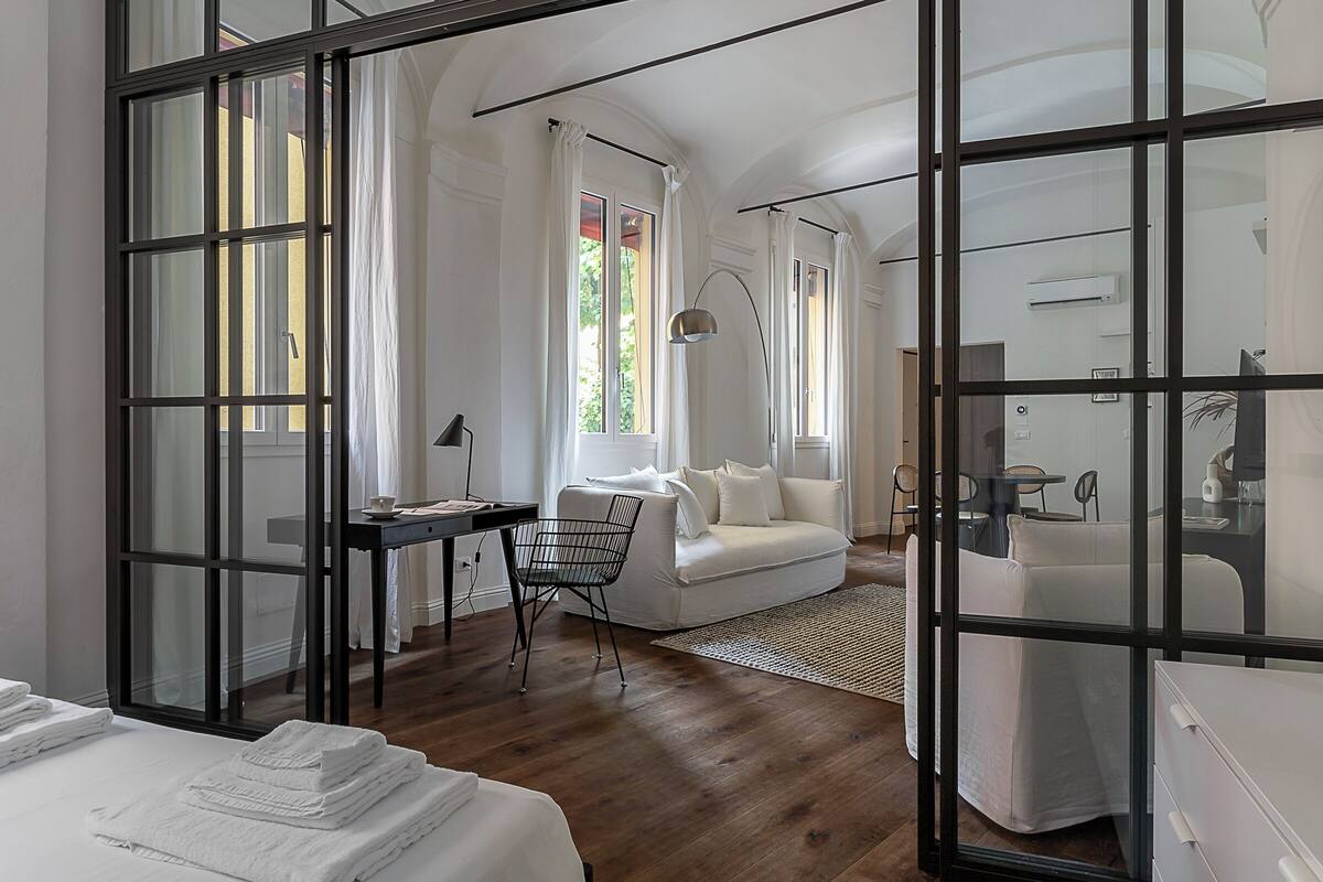 Une chambre d’hôtel moderne dotée d’une grande fenêtre, d’un bureau, d’un canapé blanc et d’un lit agrémenté de serviettes blanches soigneusement pliées.