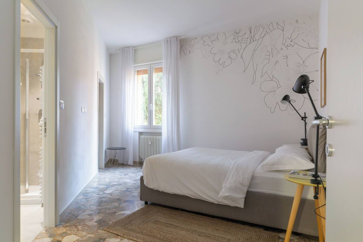 Une chambre à coucher avec un lit, une lampe sur pied, un radiateur et une fenêtre avec des rideaux.