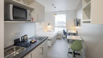 A compact hotel room with a kitchenette, a bed, a desk, and a chair.