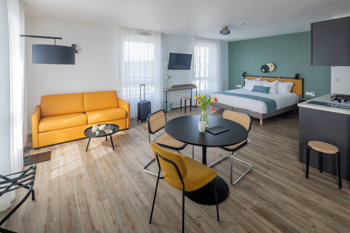 Une chambre d’hôtel moderne équipée d’un canapé, d’une table à manger, de chaises, d’un lit, d’une télévision et d’un bureau.