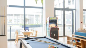 A pool table with a pool cue, a table tennis table, and an arcade game in a bright room with large windows. - All Suites Appart Hôtel | Le Havre Centre - Les docks (Le Havre)