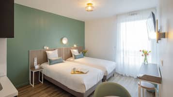 Quarto de hotel com duas camas, uma escrivaninha, uma cadeira, uma TV e uma janela com cortinas.
