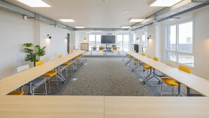 A conference room with long tables, yellow chairs, a large screen, and large windows. - All Suites Appart Hôtel | Le Havre Centre - Les docks (Le Havre)