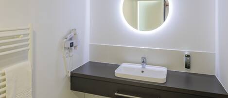 A bathroom with a white sink, a round mirror with a light, a towel rack, and a heater.