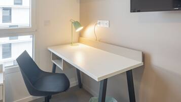 Een moderne kantoorruimte met een wit bureau, een zwarte bureaustoel en een groene afvalbak.