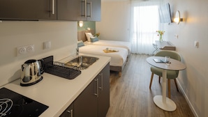 A modern hotel room with a kitchenette, a bed, a small dining area, and a TV mounted on the wall. - All Suites Appart Hôtel | Le Havre Centre - Les docks (Le Havre)