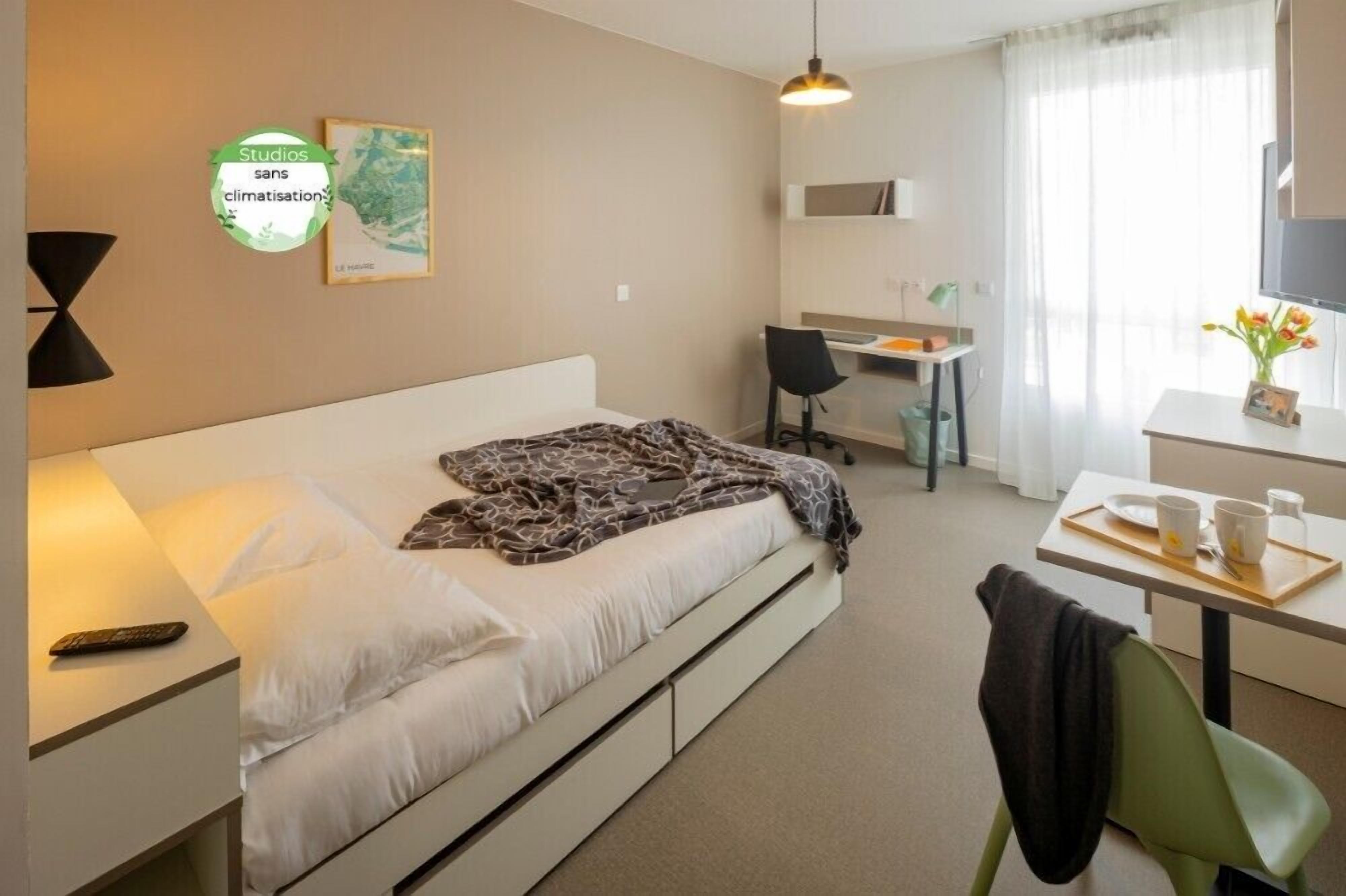 Ein Hotelzimmer mit Bett, Schreibtisch, Stuhl und einem kleinen Tisch mit Tablett.