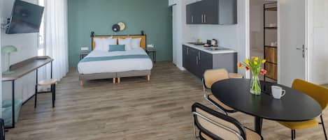 A hotel room with a bed, a desk, a chair, a dining table, and a kitchenette.