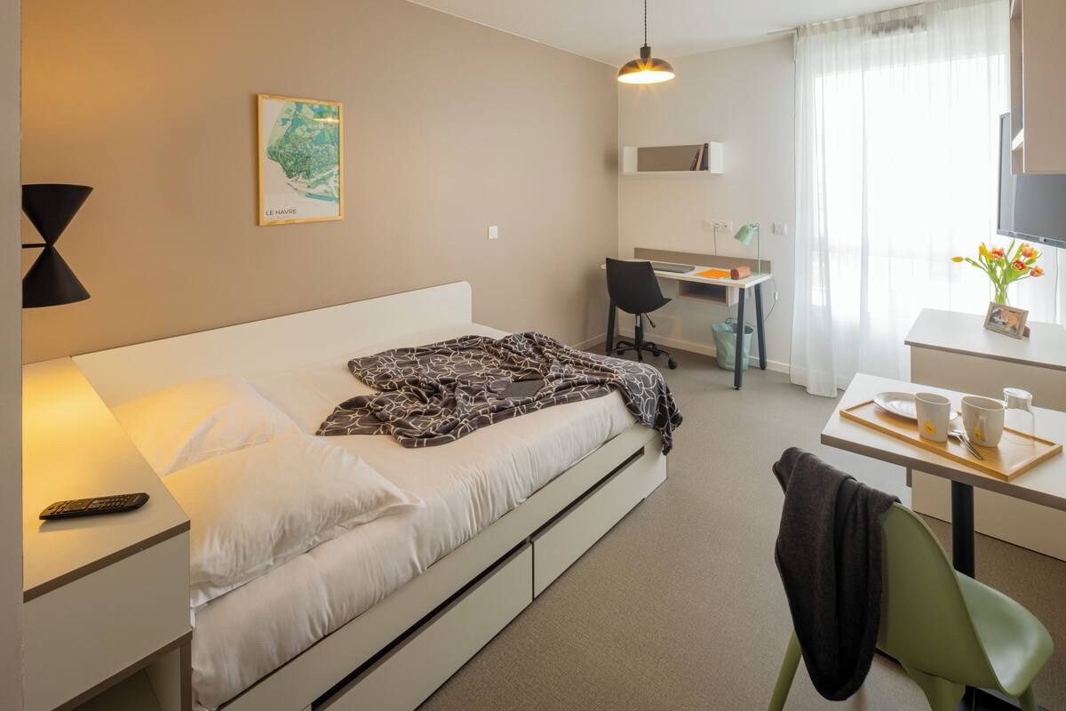 Une chambre d’hôtel comprenant un lit, un bureau, une chaise et une petite table avec un plateau.