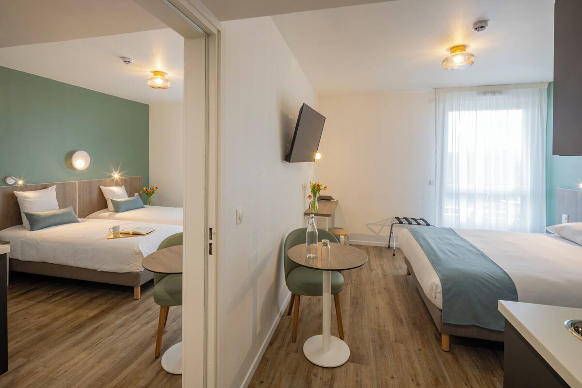 Une chambre d’hôtel moderne équipée de deux lits, d’une table à manger et d’un téléviseur fixé au mur.