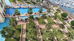 An aerial view of a resort with a central swimming pool, palm trees, and a marina with boats. - Marina Residences 2 501 (Dubai)