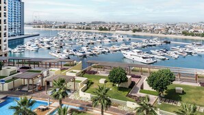A marina with numerous boats docked, a large building to the left, and a pool area in the foreground. - Marina Residences 2 501 (Dubai)