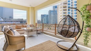 A balcony with wicker furniture, a hanging chair, and a view of tall buildings. - Marina Residences 2 501 (Dubai)
