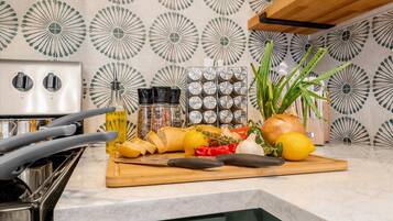 A kitchen counter with a cutting board, various vegetables, a bottle of oil, and a spice rack.