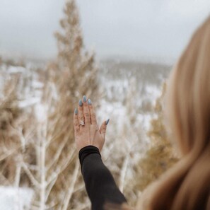 A hand with a ring, reaching out towards a snowy landscape with trees. - Theater Dome | Stargazing Hot Tub Hammock Terrace (Bailey)