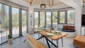 A dining area with a long table set for a meal, a bench, and a sofa with a cushion. - Villa Tolena by Marilena Pagkrati (Corfu)